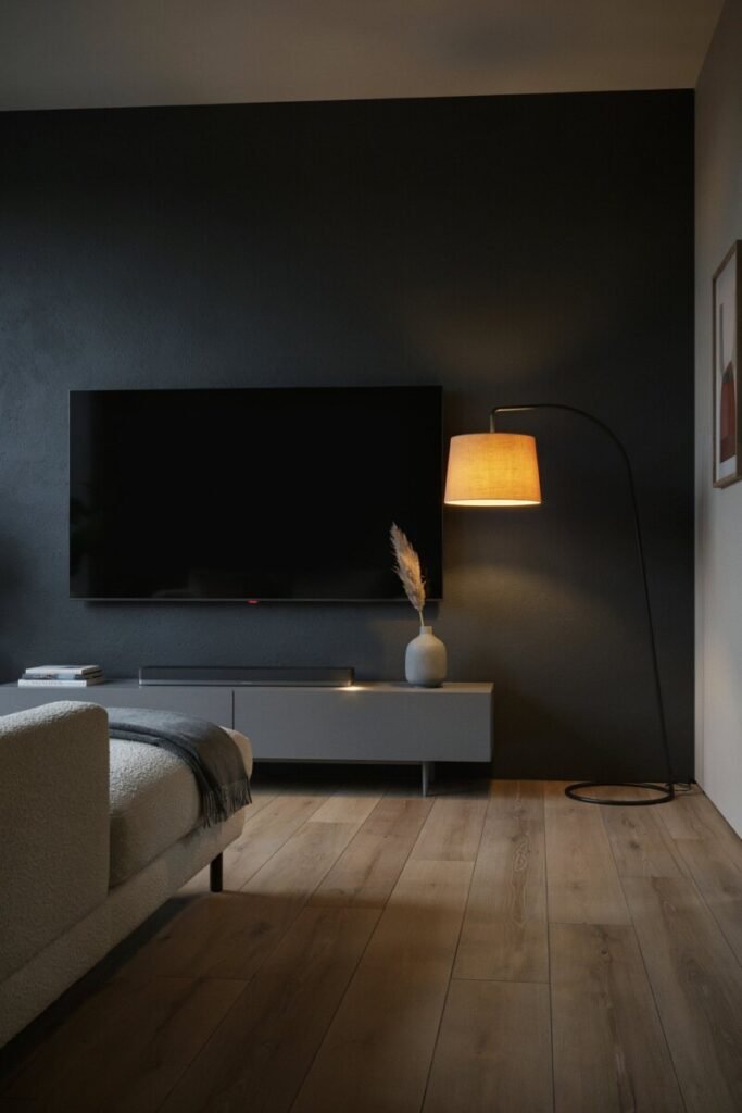 A matte black TV accent wall where the switched-off screen nearly disappears, warmed by a single 2700K floor lamp.